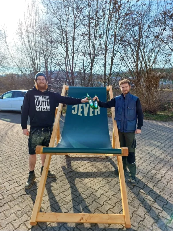 Zwei Personen vor dem JEVER XXL-Holzliegestuhl